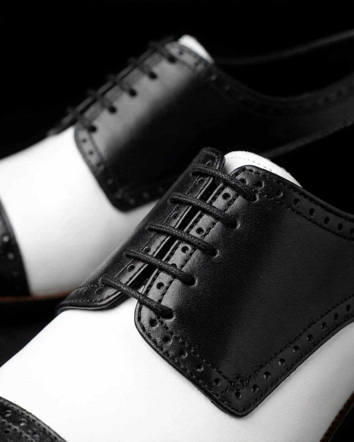 Bold & Brogue Close-up of black and white two-tone brogue shoes showing leather laces and perforated detailing