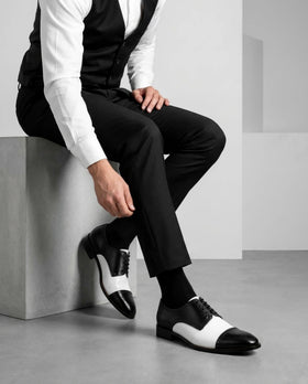 Editorial shot of Bold Brogue black and white dress shoes styled with suit in urban setting representing luxury formal footwear