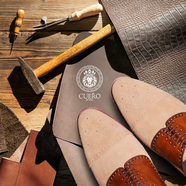 Cueřo beige suede and cognac leather men’s dress shoes displayed with traditional shoemaking tools in an artisan workshop