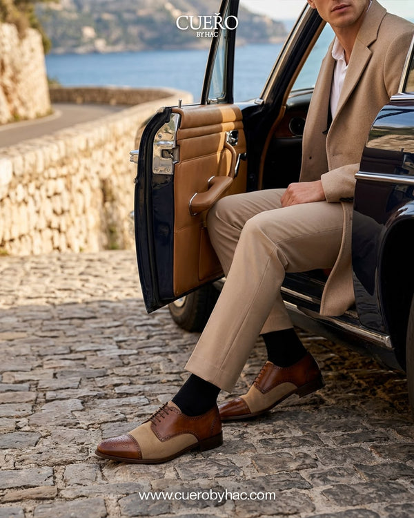 Man in a beige suit wearing Cueřo tan and brown two-tone brogue dress shoes beside a luxury car on a coastal road