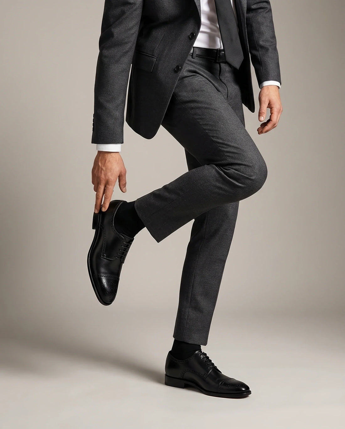 Person wearing a gray suit and Regal black shoes on a plain background